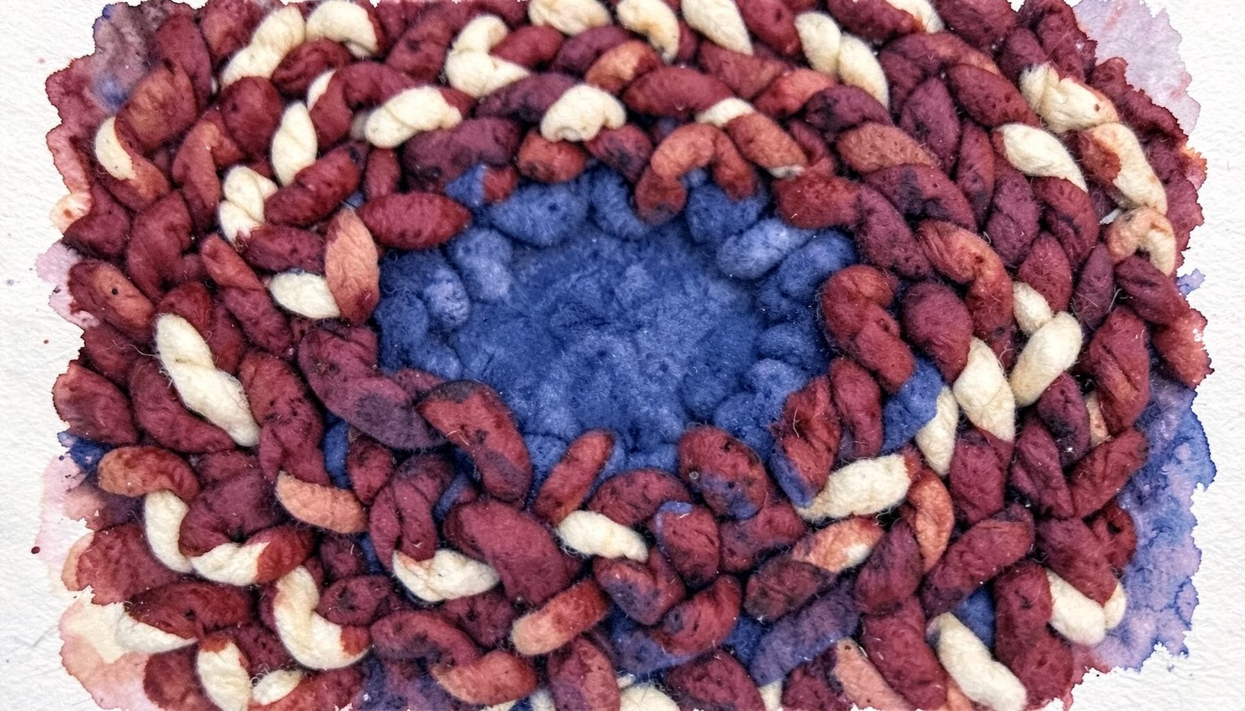A close view of a hand-looped wool rug in warm burgundy and cream tones, showing rich looped texture