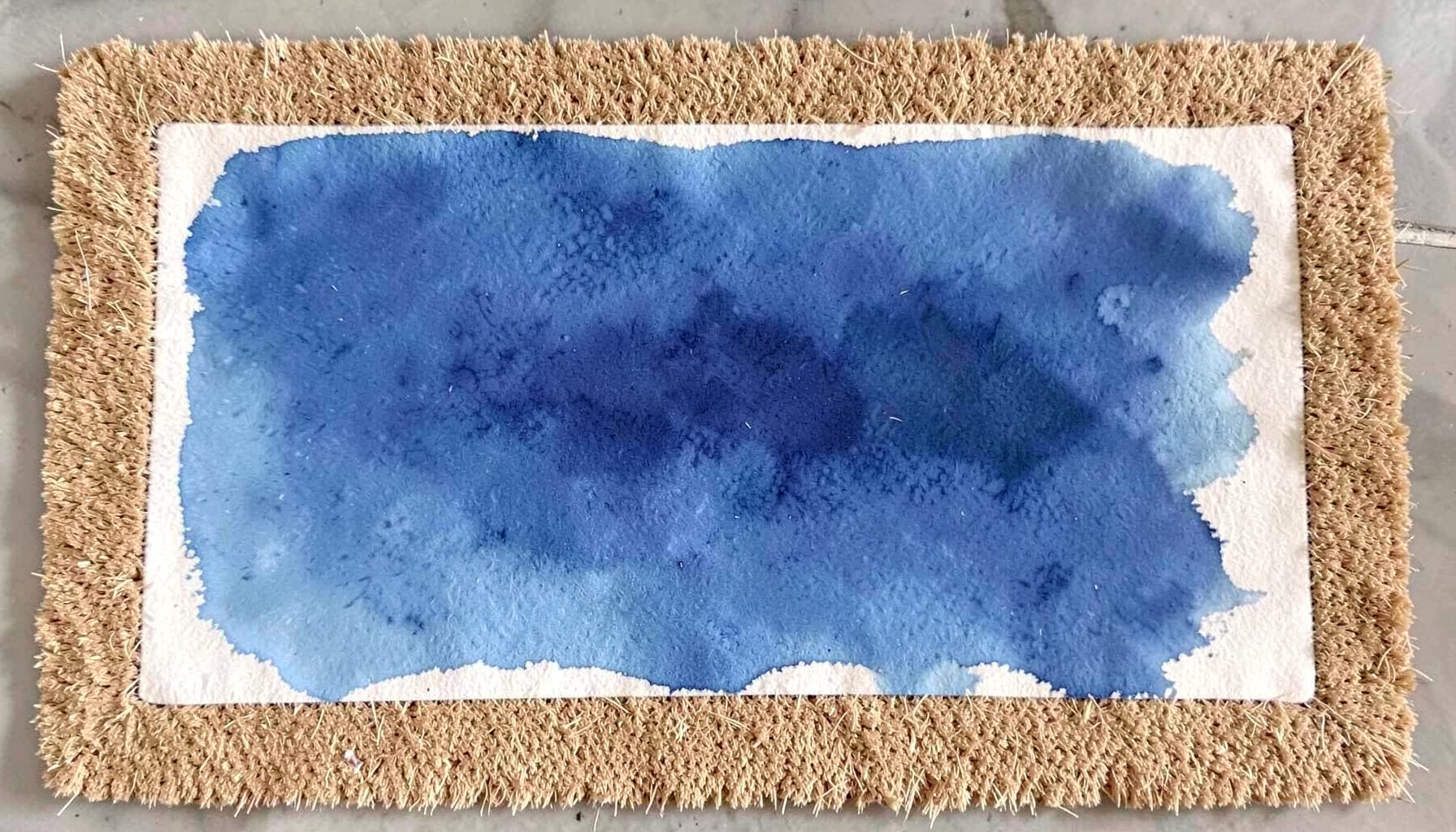 A natural fiber doormat with coarse coconut coir bristles and a simple stenciled border