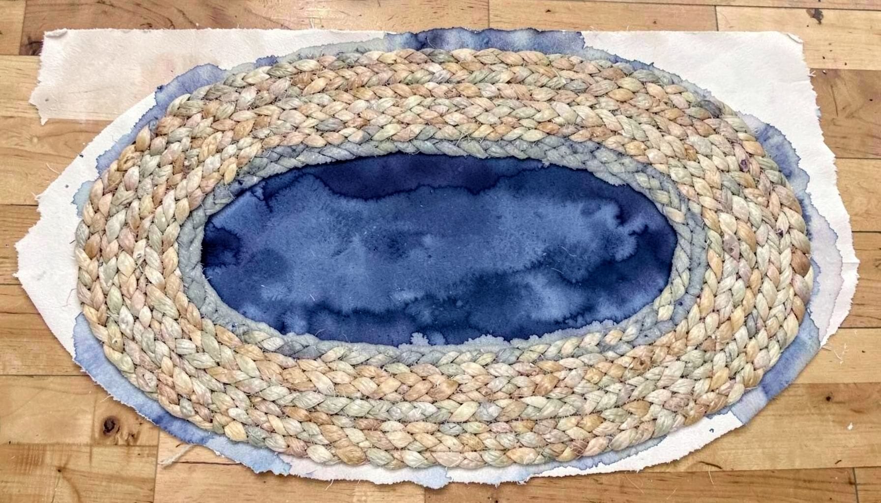A braided jute rug in concentric oval rings of natural tan and oatmeal fibers on a wood floor