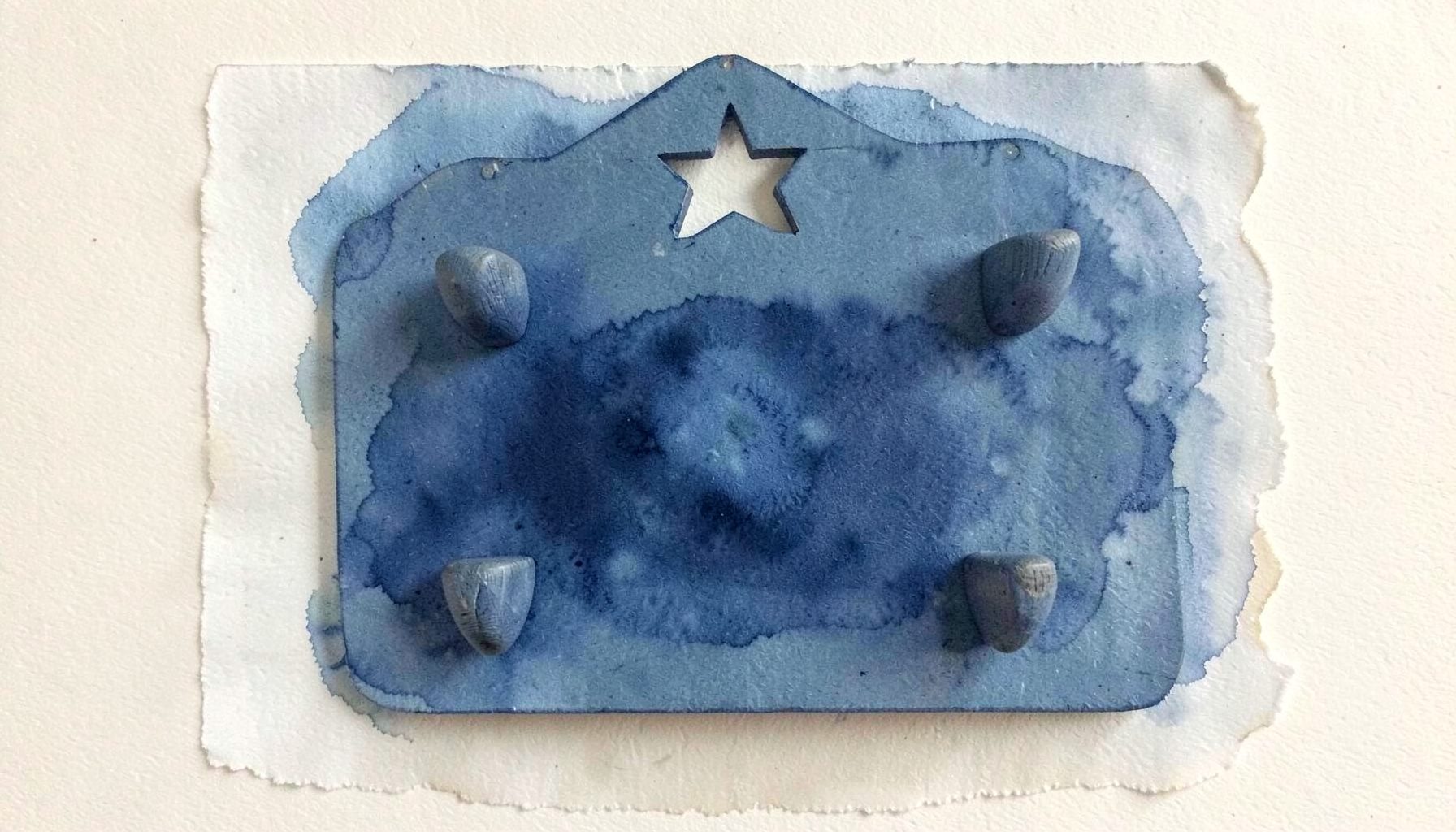 A wooden mitten rack with four pegs and a star cutout at the top, painted in muted colonial blue, mounted on a cream wall